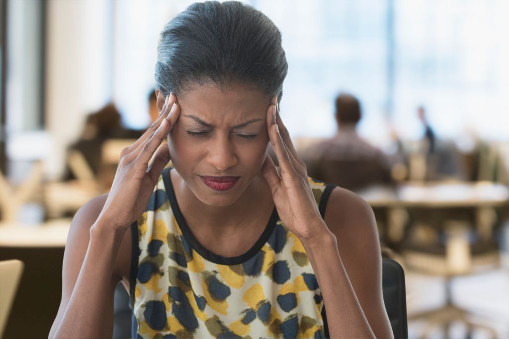 Anxious mixed race businesswoman rubbing temples in office