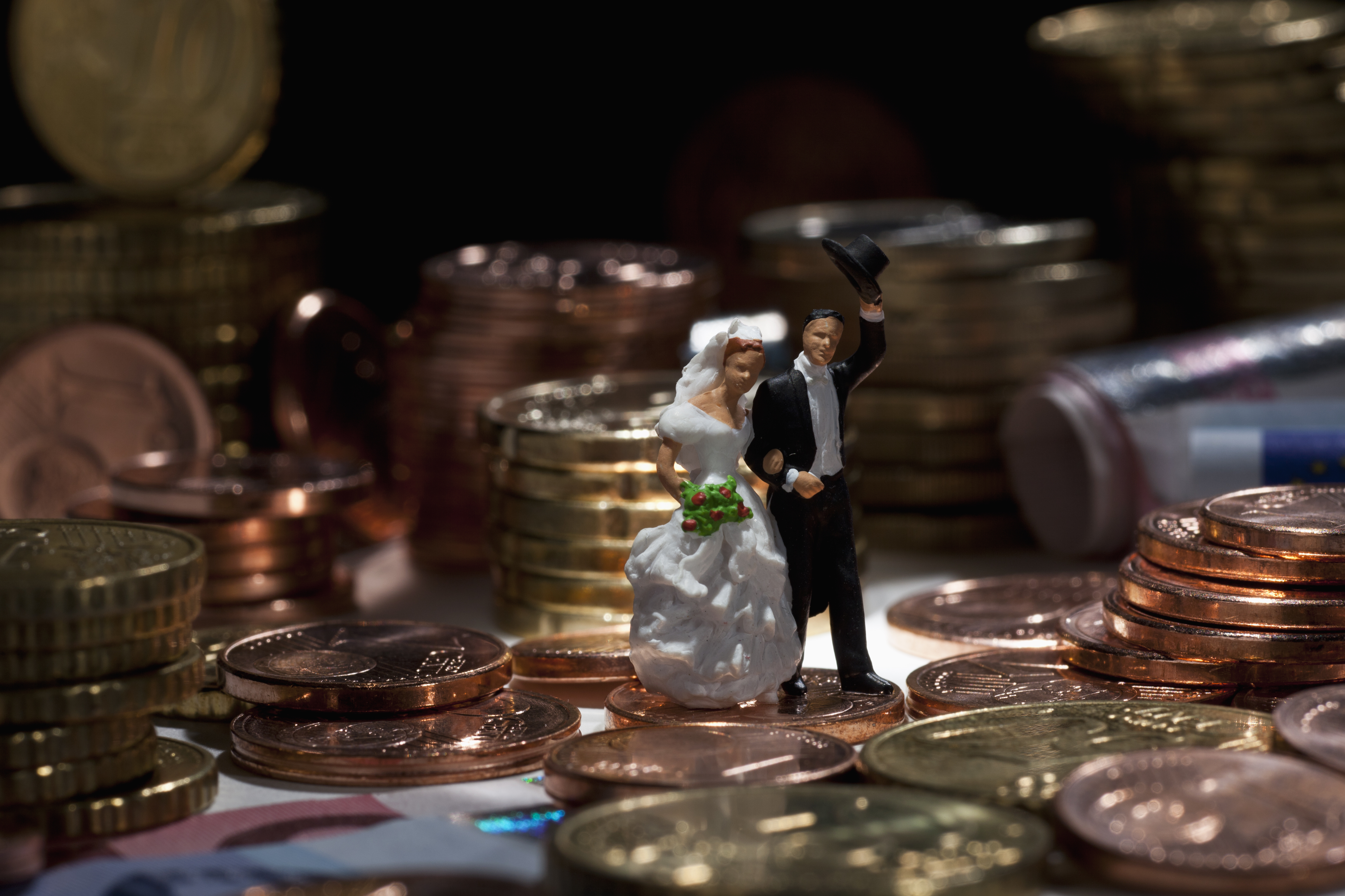 Miniature wedding couple figurines amidst stacks of European Union coins