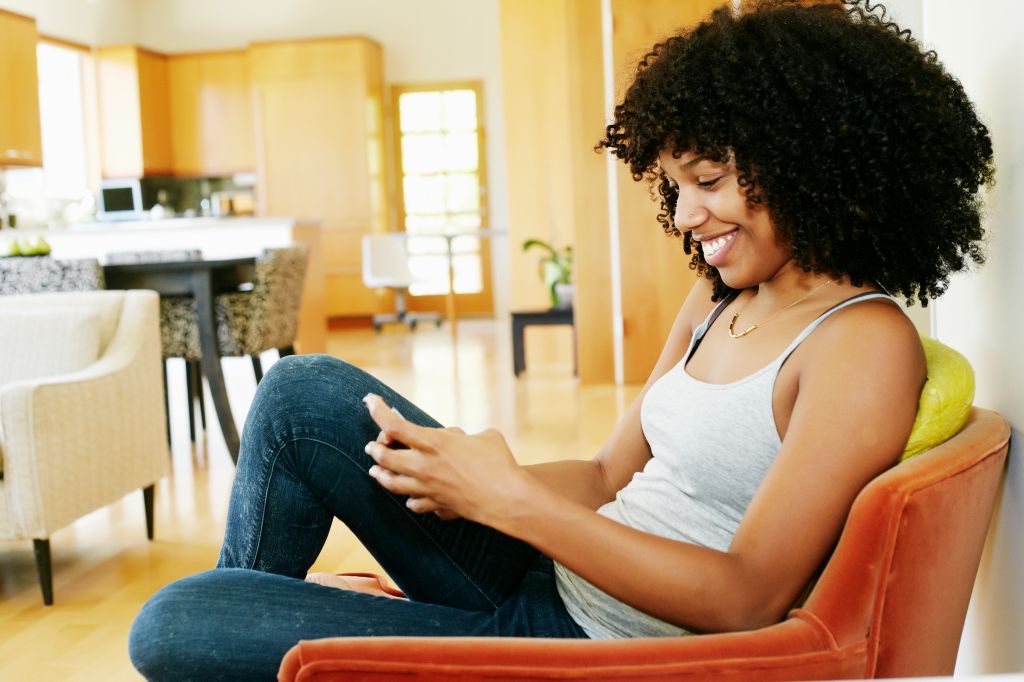 Mixed race woman using cell phone in armchair