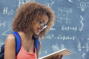 High school student reading homework assignment in front of blackboard