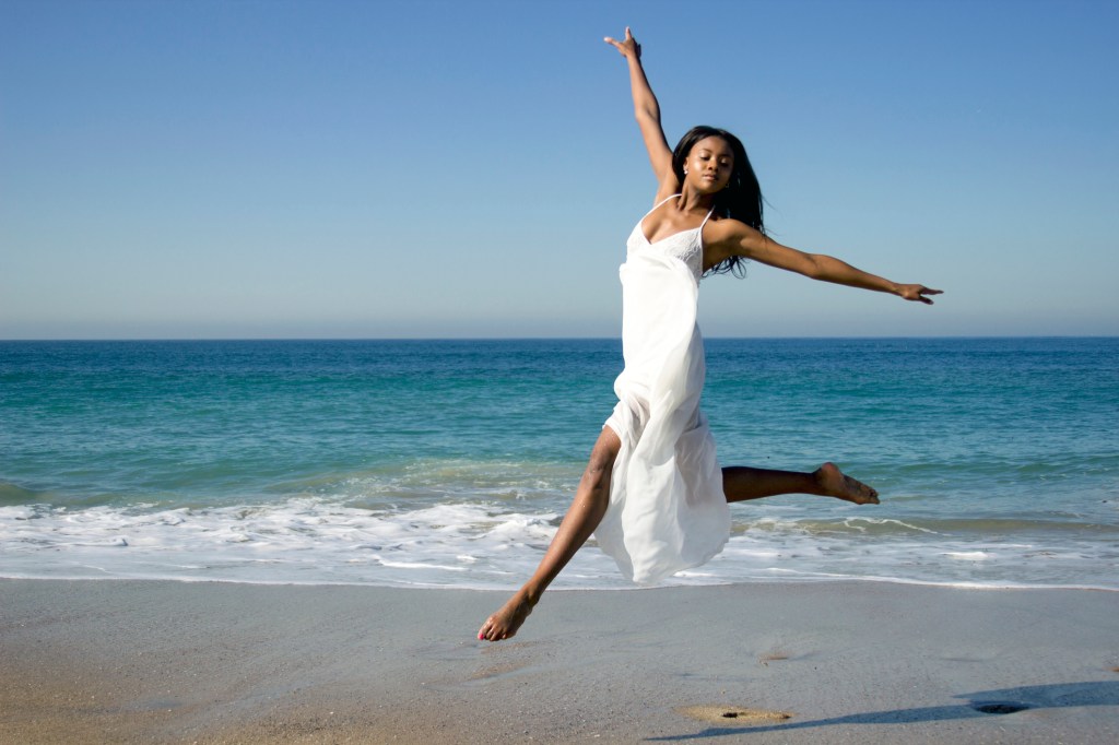 Young female dancer leaping mid air on beach
