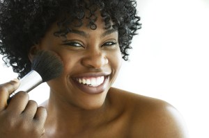 Young woman using make-up brush, smiling, portrait, close-up