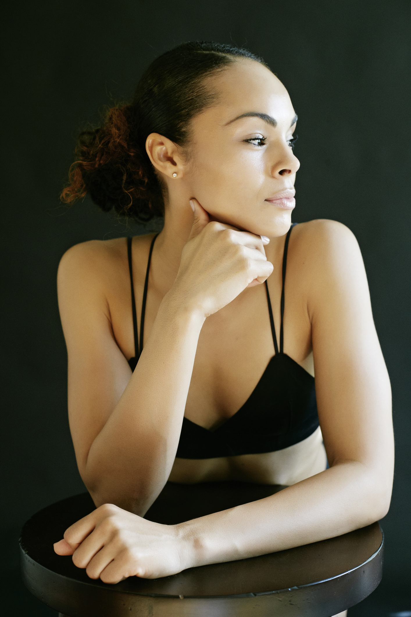 Pensive Mixed Race woman wearing bra leaning on stool