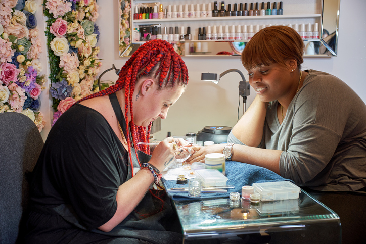 A nail artist and her client having her nails manicured.
