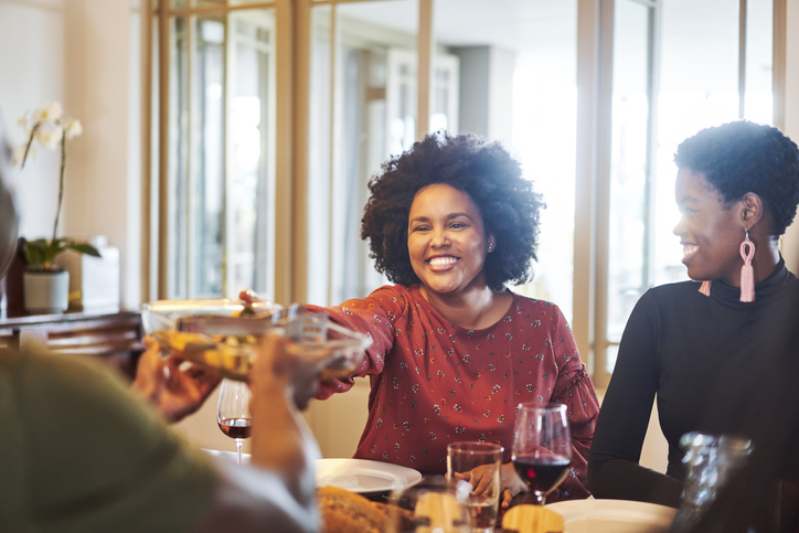 Smiling woman passing food to friend at table