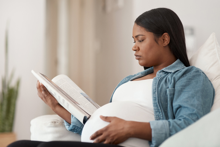 Shot of a pregnant woman reading a book at home