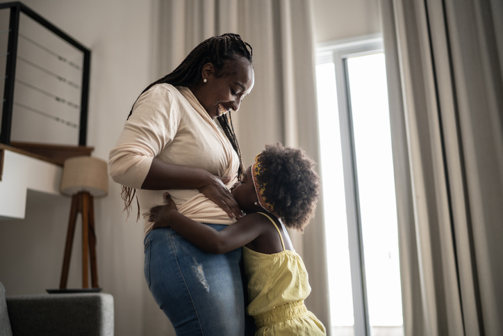 Girl kissing her pregnant mother's belly at home