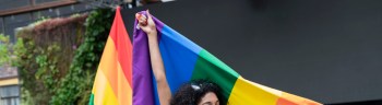 Portrait of a brunette Latina with curly hair enjoying her gay pride day dressed very colorful smiling at the camera while happily holding her gay pride flag