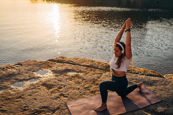 Flexible woman doing yoga on the beach. She performs a sun salutation yoga pose