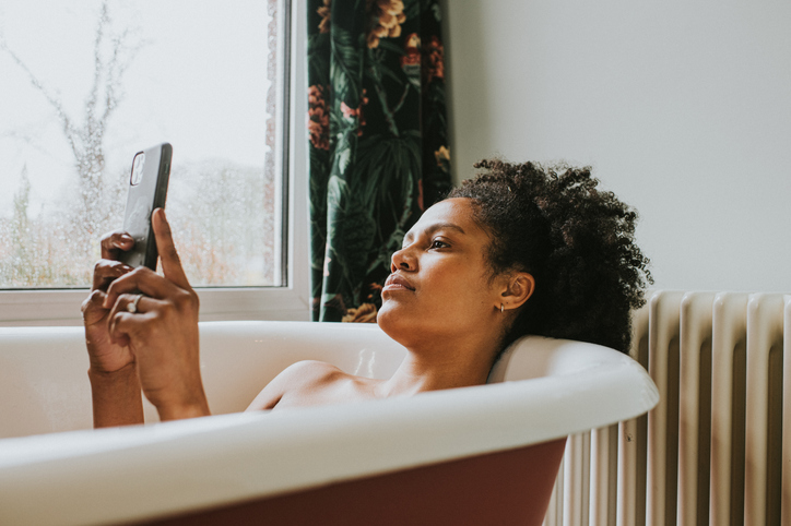 A relaxed woman uses her smart phone as she bathes in a luxurious roll-top bath