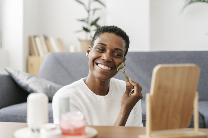 Smiling woman using jade roller and looking in mirror at home