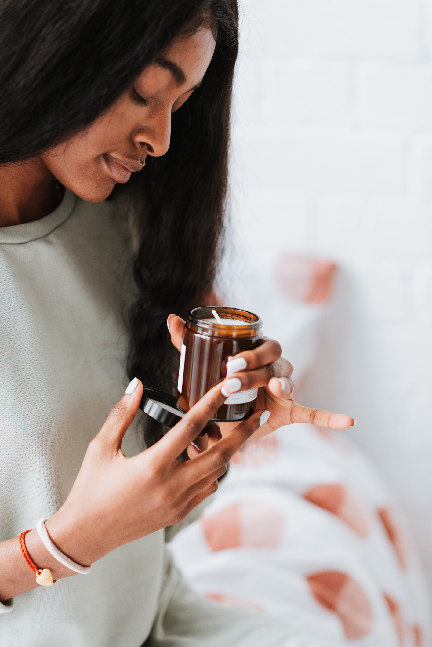 Pretty young African female with long black hair holding a glass jar with a handmade scented candle
