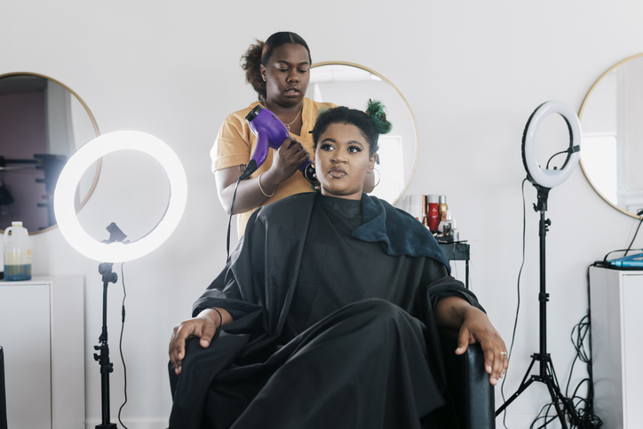 Black Woman Sitting In Chair Getting Hair Styled By Her Hairdresser