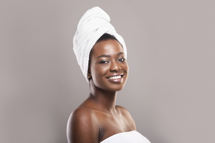 Beautiful black woman with towel on head over grey background