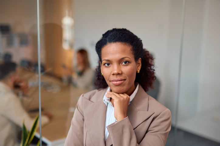 Confident businesswoman posing in modern office with team working in background