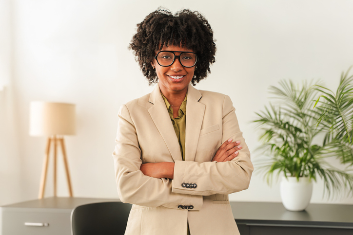 Confident businesswoman with glasses smiling while standing with arms crossed in a stylish suit